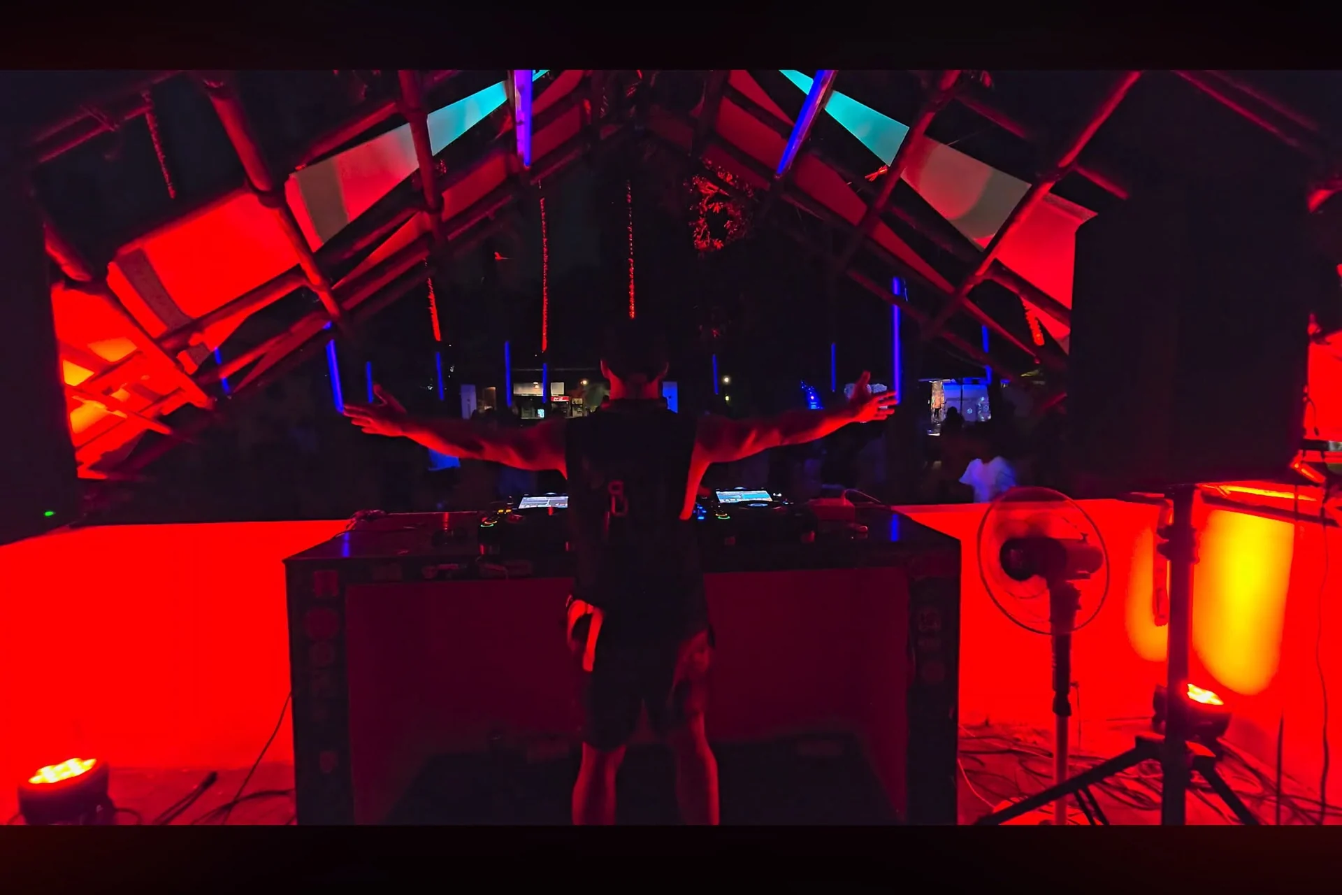 Kevin Em performing behind the decks under red and blue lights